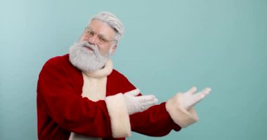 Şık, modaya uygun Noel Baba mavi arka plan stüdyosunda yalnız poz veriyor. Yan tarafı gösteriyor, reklamlar, sunumlar.