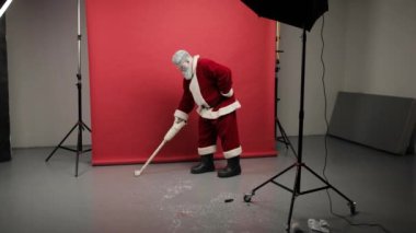 Noel Baba yerden elektrikli süpürgeyle şeker topluyor. Şık Noel Baba çekimlerden ya da tatilden sonra fotoğraf stüdyosunu temizler..