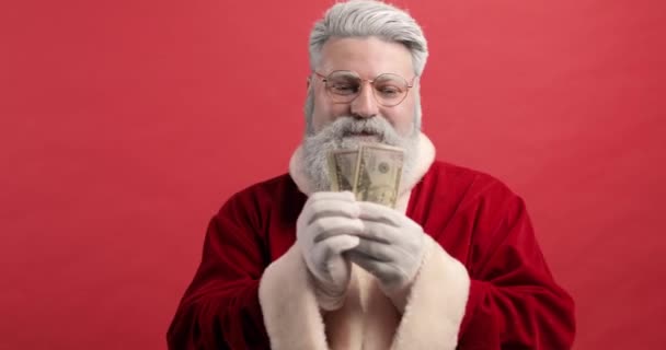 Legrační Stylový Santa Claus na červeném pozadí drží peníze dolarů v rukou. Finance, peníze, bankovky. Detailní záběr — Stock video