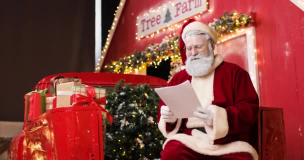 Porträt eines niedlichen Weihnachtsmannes beim Lesen von Briefen in einem wunderschönen, zum Jahreswechsel dekorierten Studio. — Stockvideo