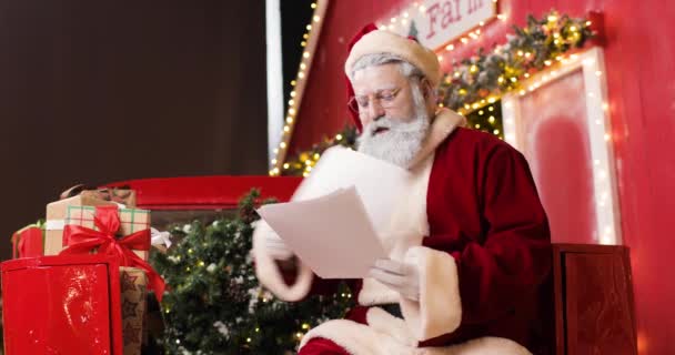 Porträtt av en arg jultomte läsa brev i en vacker nyår dekorerad studio. Han kastar bort och river upp några av breven. — Stockvideo