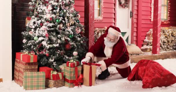 Santa Claus puts boxes of gifts from big sack under Christmas tree on Christmas Eve or New Year Eve. Beautiful New Years decorated studio. — Stock Video