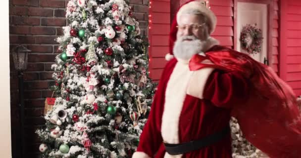 Szczęśliwy Święty Mikołaj w pośpiechu życzy wszystkim ludziom szczęśliwego Nowego Roku, patrząc w kamerę i machając ręką na tle pięknego Nowego Roku urządzone studio. — Wideo stockowe