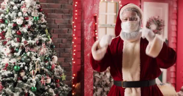 Potret Santa Claus dalam topeng pelindung dan sarung tangan dengan latar belakang sebuah studio tahun baru yang indah dan pohon Natal. Santa melepas topeng dan membuangnya.. — Stok Video