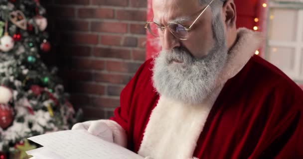 Close-up Santa Claus zadziwiająco czytania listów w pięknym noworocznym studio urządzone. — Wideo stockowe