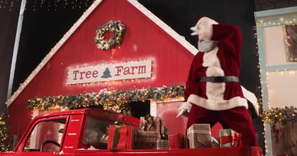 Funny Santa Claus está bailando en un estudio decorado de Año Nuevo en un camión rojo con regalos de Año Nuevo cerca de un árbol de Navidad con luces. Celebraciones y concepto de personas alegres. — Vídeos de Stock