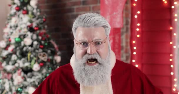 Portrét vzteklého zuřivého Santa Clause v brýlích, jak něco křičí a vyhrožuje na pozadí krásného novoročního červeného domu, se světly a vánočním stromečkem. — Stock video