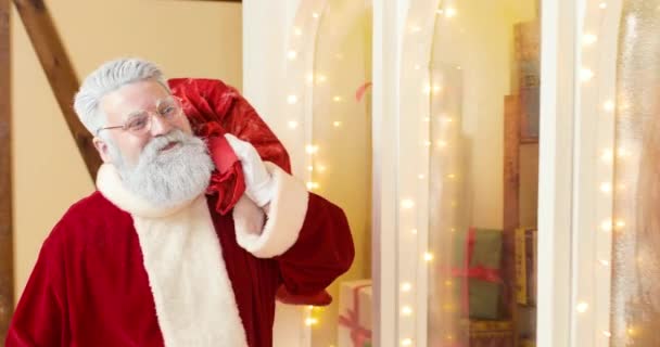 Der Weihnachtsmann mit einem großen Sack voller Geschenke geht zum Silvester geschmückten Haus und klopft an die rote Tür. — Stockvideo