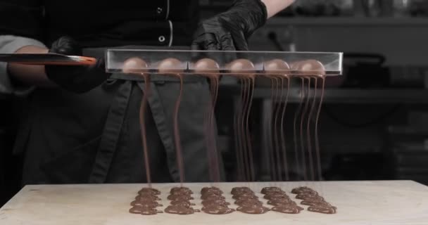 Gros plan - mains du chef, dans des gants noirs, en versant magnifiquement du chocolat ou de la crème au chocolat à partir de petits moules sur la table. — Video