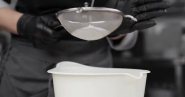 Un bir elekten geçiriliyor. Hamur işi şeflerinin elleri siyah eldivenler, un eleme veya pudra şekeri.