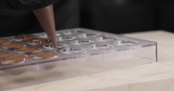 Chocolade of chocolade crème wordt gegoten in speciale kleine schimmels uit een culinaire zak. Een close-up. Een close-up. Chocolatiers maken handgemaakte biologische chocolade. — Stockvideo