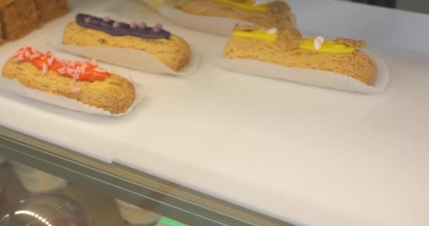 Close-up of womans hands in gloves putting ready-made eclairs on the shop window. — Stock Video