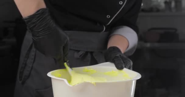 Chefs handen in zwarte handschoenen roeren room, boter of deeg in een witte kom. Close-up. — Stockvideo