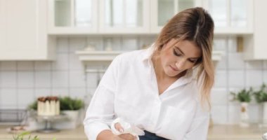 Bir kadın hamur ya da kremayı hamur torbasından çıkarıp pastacı beyaz mutfağında parşömen kağıdına sıkıştırıyor. Video taşınıyor.