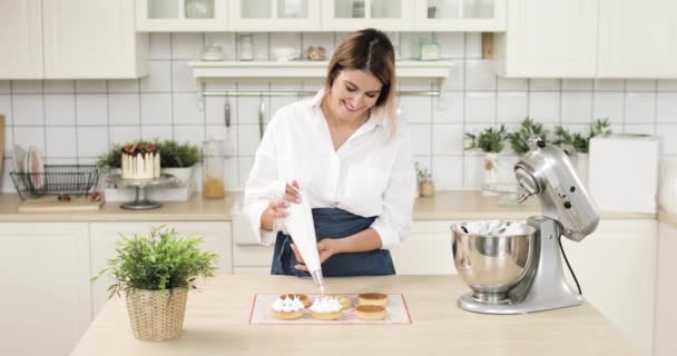 Portrait of a young woman pastry chef decorating biscuit tartlet with cream from pastry bag. Preparation of cake at home bakery with piping bag. — Stock Video