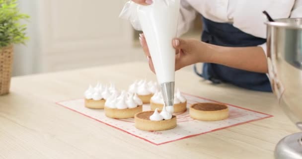 一个年轻的女糕点厨师用糕点袋中的奶油装饰饼干块的手。特写。在家里烘焙蛋糕. — 图库视频影像