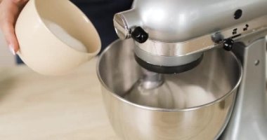 Baker malzemeleri kasede karıştırıyor hamur hamuru pişiriyor elektrikli karıştırıcı kullanıyor, şeker ekliyor, yakın plan çekiyor. Pişirme ve şekerleme adımları.