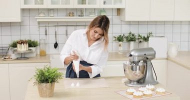 Bir kadın hamur ya da kremayı pastanenin beyaz mutfağında kağıt parşömen kâğıdına sıkıştırıyor..