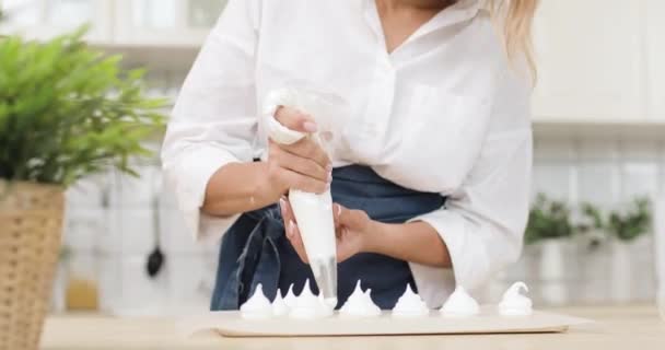 Een vrouw perst het deeg of de room uit een banketbakje tot perkamentpapier in de witte keuken van de banketbakkerij. Close-up van de handen. — Stockvideo