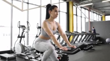 Güzel, genç, esmer bir kadın spor salonunda egzersiz bisikletinde kardiyo yapıyor..