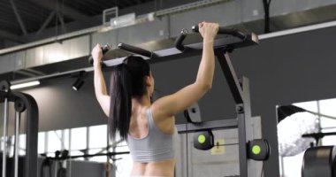 Spor kıyafetleri giymiş genç bir esmer kadın spor aletleri, omuzlar, pazılar ve spor salonunda egzersiz yapıyor. Arka plan.