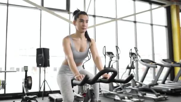 Hermosa joven caucásica haciendo cardio en una bicicleta de ejercicio en el gimnasio. — Vídeo de stock