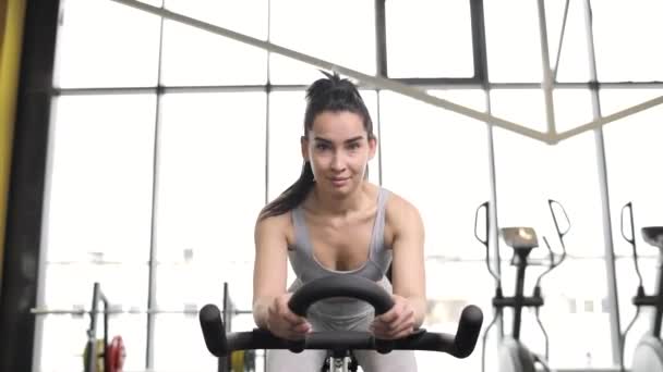 Portrait of a beautiful young brunette woman doing cardio on a exercise bike at gym. — Video Stock