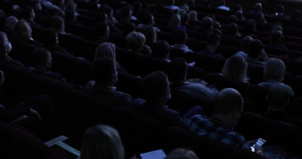 Back view of the audience sitting at a business conference. Subdued light in the hall. Business people is listening a presentation of lector. — Wideo stockowe