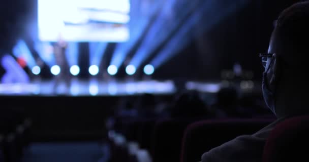 Back view between the rows of the audience sitting at a business conference. Focus is on the one man with protective mask on his fase. — Video Stock