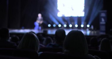 Seyircilerin bir iş konferansında arka planda oturması. Koridorda bastırılmış ışık. Sözcü, diğer iş adamlarından oluşan farklı bir gruba sunum yapacak.