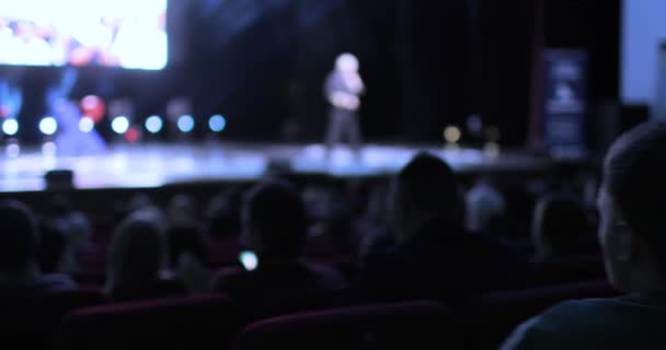 Tylny widok publiczności siedzącej na konferencji biznesowej. Kamera przesuwa się od tyłu widowni na scenę, pokazując mówcy. — Wideo stockowe