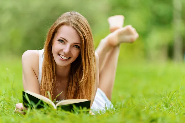 Mladá žena ležící na trávě a čtení knihy — Stock fotografie