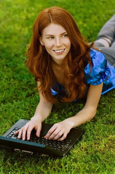 Junge Frau liegt mit Laptop im Gras — Stockfoto