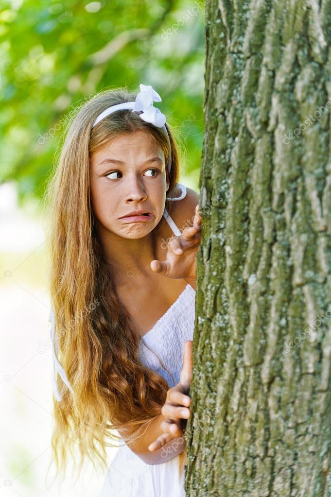 frightened teenage peeping from behind tree