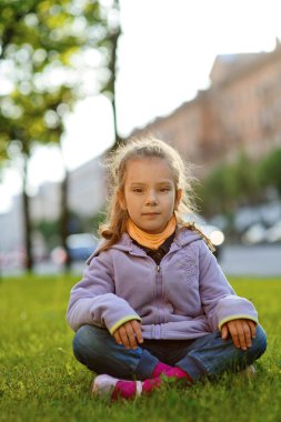 Yeşil çimenlerin üzerine oturmuş ceket, küçük kız