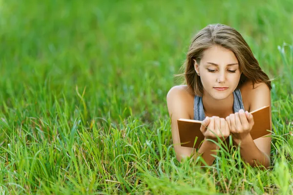 Νεαρή γυναίκα-φοιτήτρια ανάγνωση βιβλίο στο γρασίδι — Φωτογραφία Αρχείου