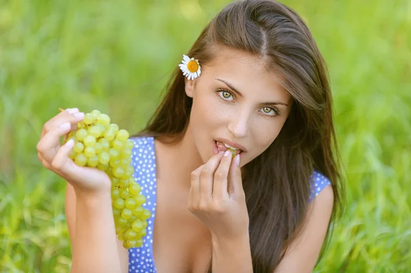 Jovem mulher sentada na grama e comer uvas — Fotografia de Stock