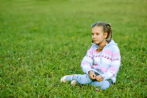 Menina bonita com tranças sentado na grama verde — Fotografia de Stock