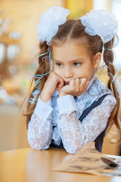 Sad girl with beautiful bows sitting at wooden table — Stock Photo, Image