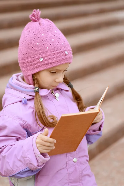 Little girl in pink coat reads book — Stock Photo, Image