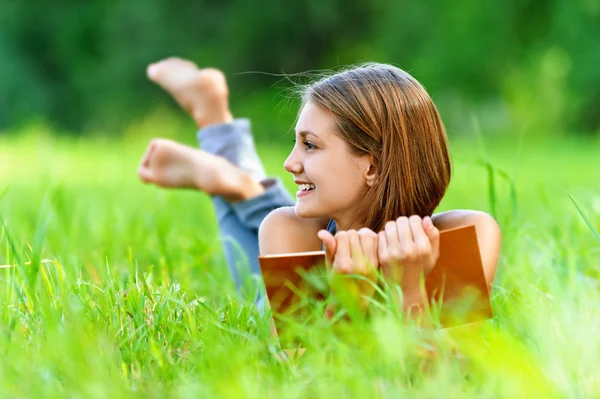 Jonge vrouw liggend op gras en boek lezen — Stockfoto