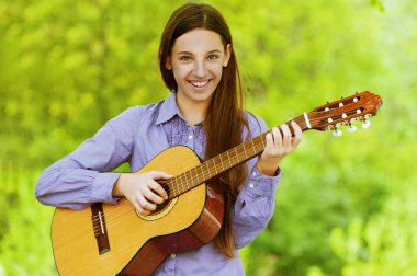 Gülümseyen genç kız gitar çalıyor.