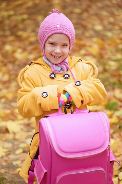 ピンクのバックパックでイエロー コートを着た小さな女の子が笑みを浮かべてください。 — ストック写真