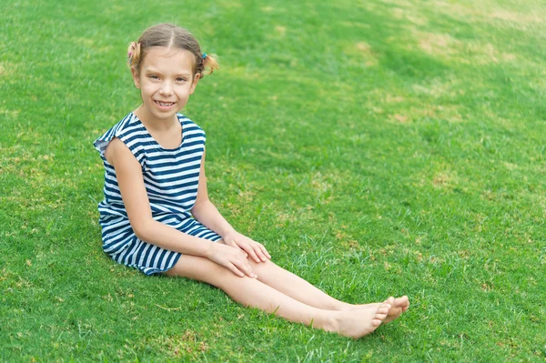 Yeşil çimenlerin üzerinde oturan güzel gülümseyen kız — Stok fotoğraf