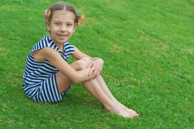 Yeşil çimenlerin üzerinde oturan güzel gülümseyen kız