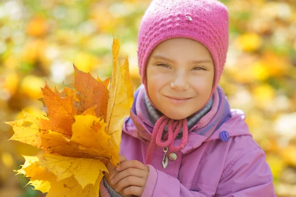Маленькая девочка в жёлтом пальто собирает листья жёлтого клена — стоковое фото