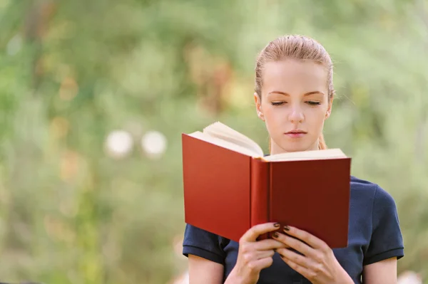 Mujer joven en blusa oscura lee libro rojo — Foto de Stock