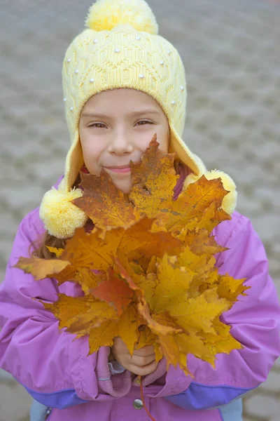 Kleines Mädchen im gelben Mantel sammelt gelbe Ahornblätter — Stockfoto