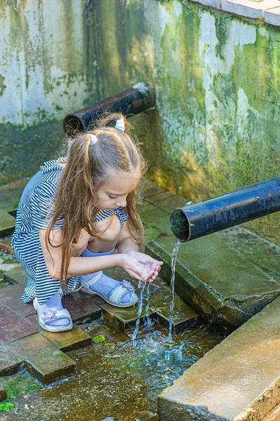 Little girl drinks water from source — Stock Photo, Image
