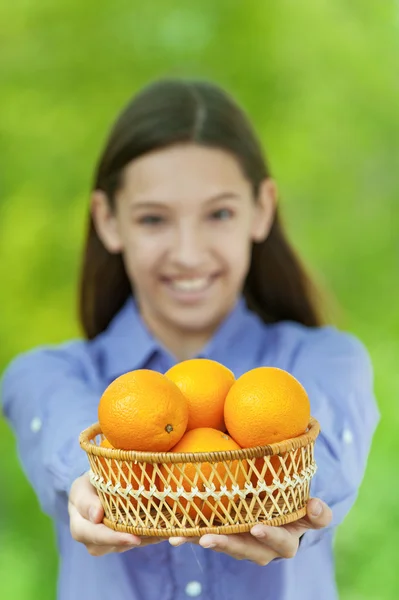 Smiling teenage girl holding basket of oranges — Stock Photo, Image